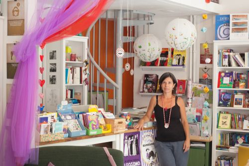 TIRITERA, la libreria della magia circense (Via Giuseppe Govone 30, Cenisio)
Cinzia si è lanciata un po’ come una trapezista in questo sogno dopo aver letto sul Corriere della Sera l’intervista alla libraia Cristina di Canio. Metafora circense d’obbligo: poco distante dalla libreria sorge la Piccola Scuola di Circo, un tendone-bomboniera dedicato alle magiche arti della pista. Un po’ una passione sottintesa e un po’ la reciproca vicinanza hanno reso la libreria un luogo pieno di citazioni circensi: illustrazioni, libri e artisti vanno e vengono facendo capolino tra gli scaffali.